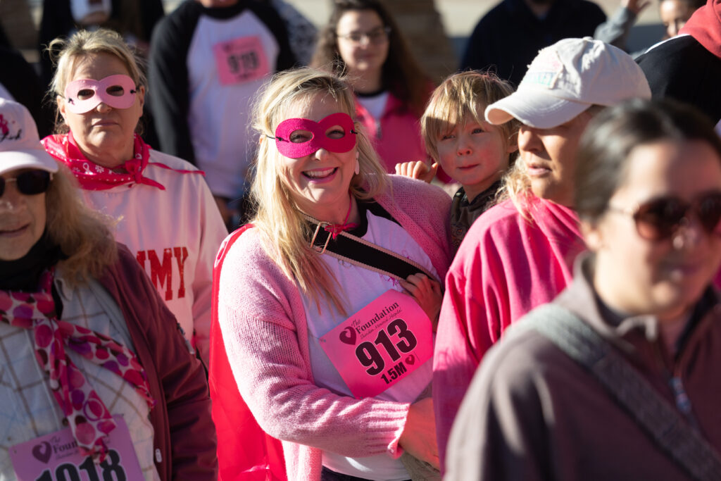 Woman in pink wearing superhero mask and holding small boy.