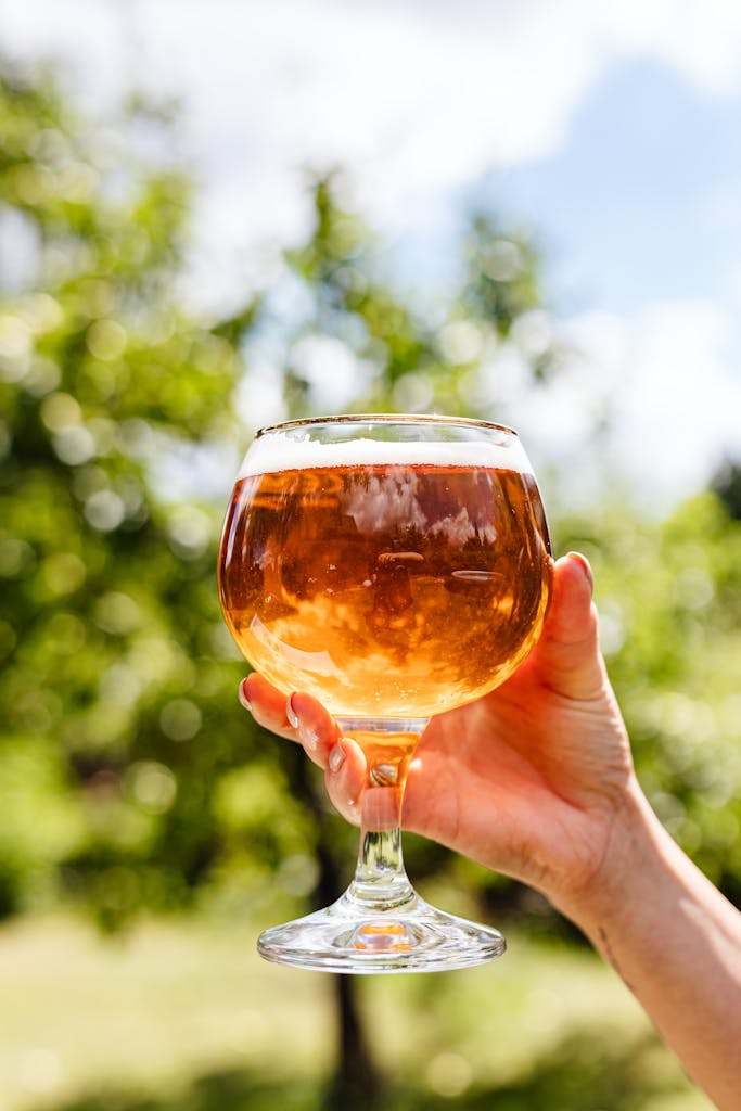 Hand holding a beer glass outdoors on a sunny day, capturing a refreshing summer vibe.